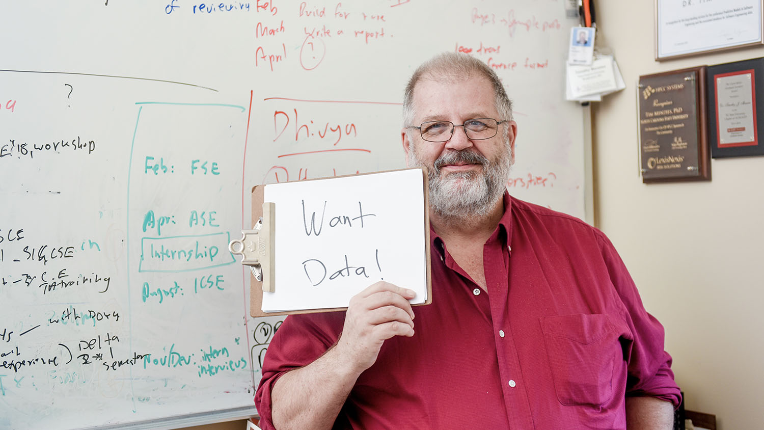 Tim Menzies, a smiling older man with a white beard, holds up a sign that says “Want Data!”