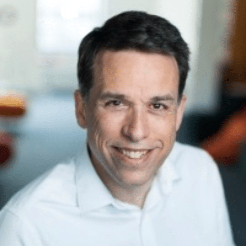Headshot of a man wearing a white shirt in front of an out of focus office background