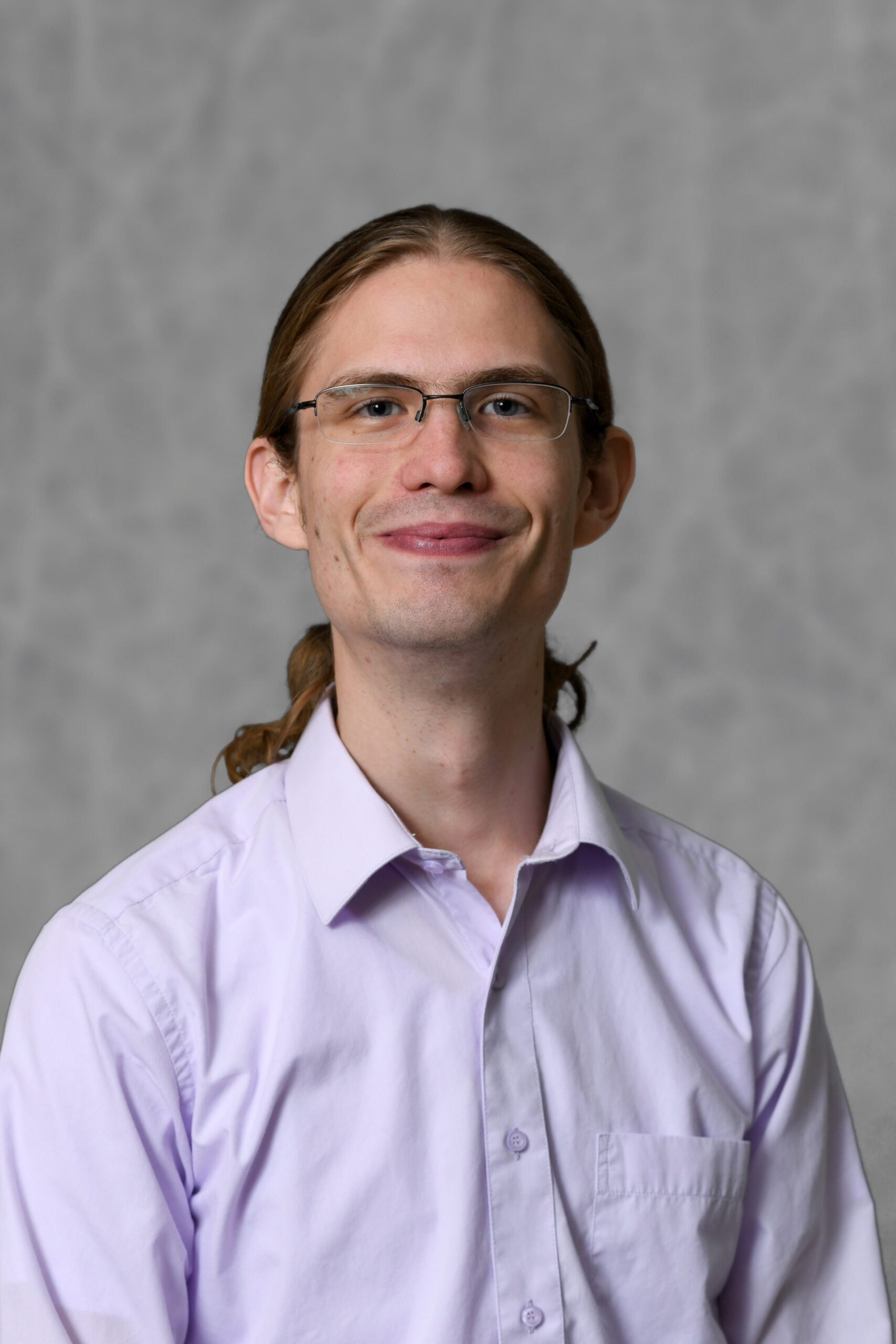 A photo of a smiling white man wearing a lavender button down shirt.