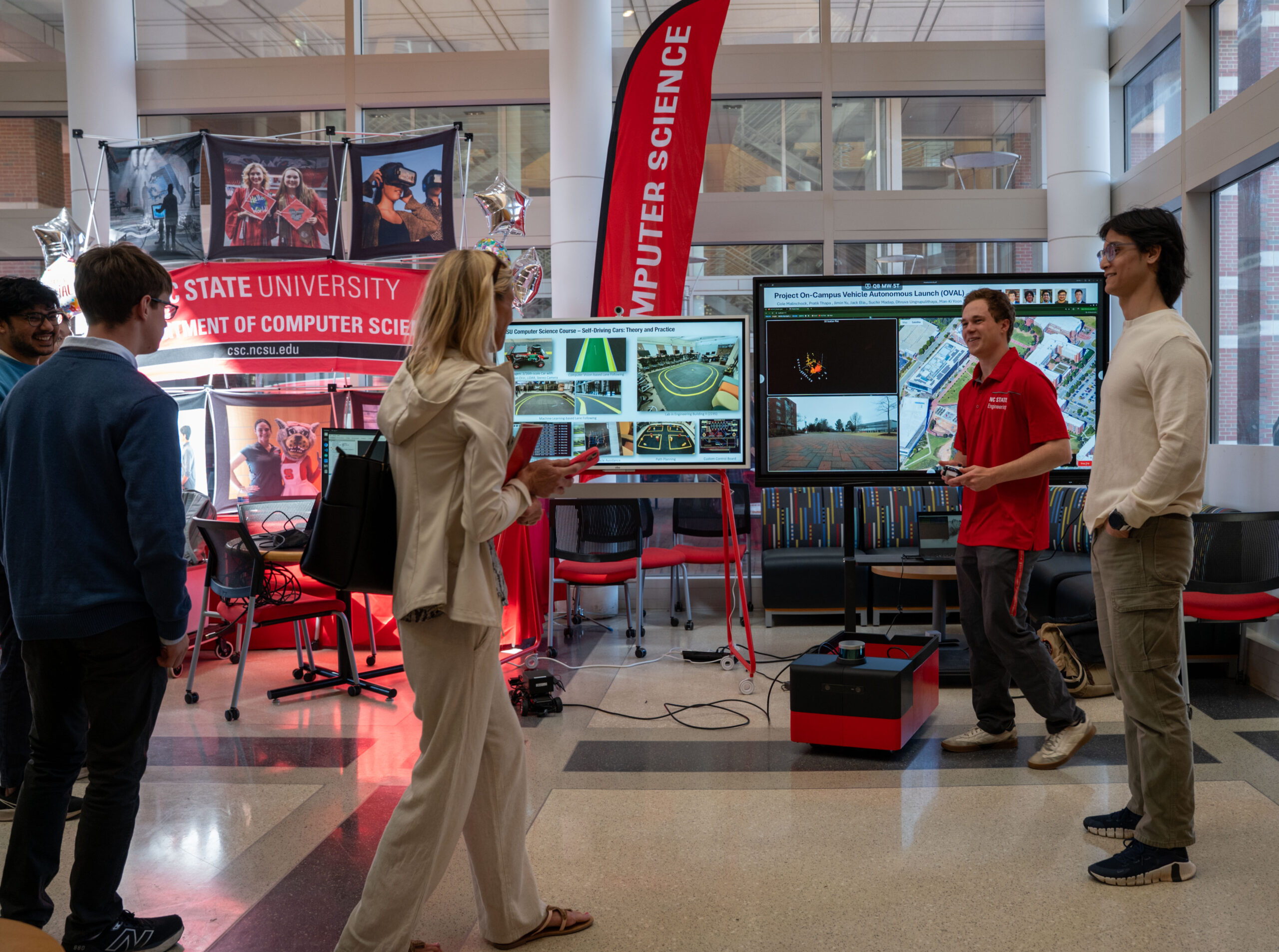 A photo of an atrium in a modern academic building. In the background, there are multiple monitors and signs saying "Computer Science"