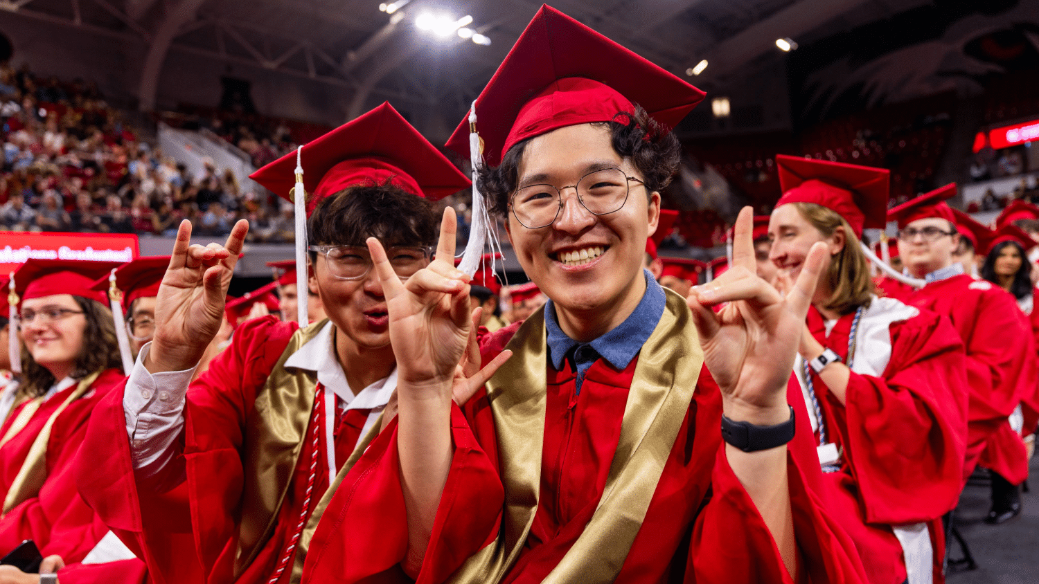 A group of graduates smiling at the camera wearing red robes at graduation
