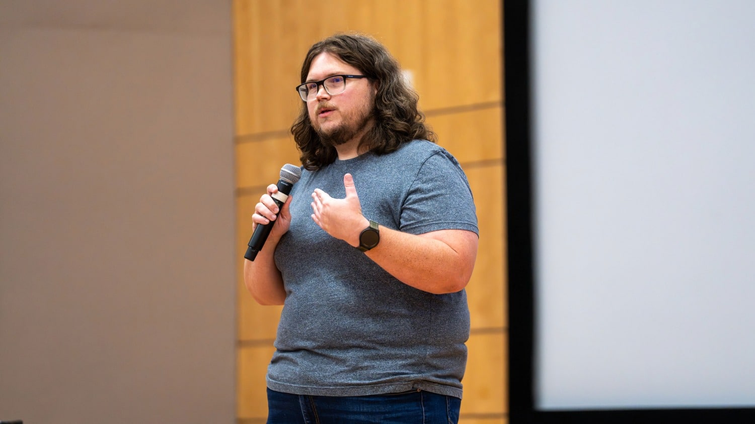 A man standing on a stage, holding a microphone and giving a lecture